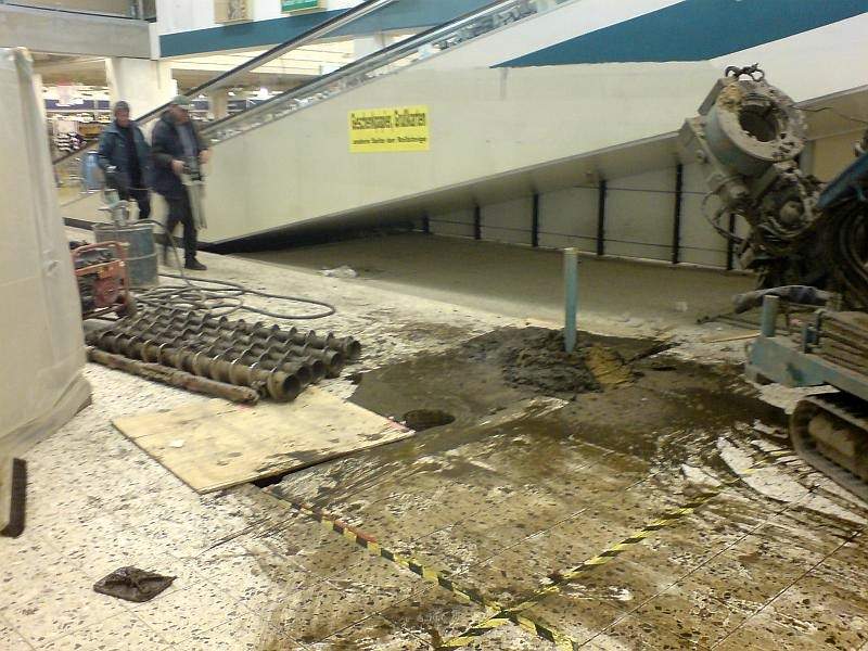 Bohrgerät mit Hohlbohrschnecke im Untergeschoss eines Kaufhauses neben einer Rolltreppe