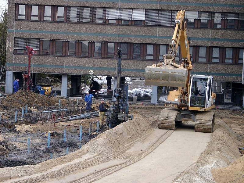Raupenbohrgerät auf einer Baustelle vor einem Gebäude, daneben ein Bagger