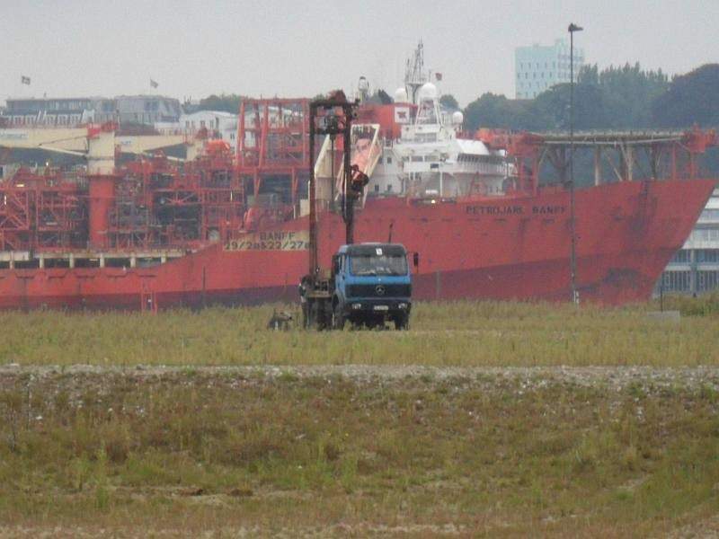 LKW-Bohrgerät vor einem roten Containerschiff im Hamburger Hafen
